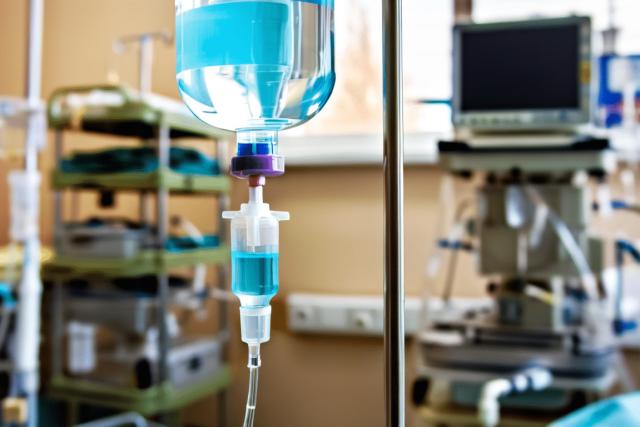 A close-up of a sterile IV drip line with fluid flowing, emphasizing its critical role in treating sepsis. The background is softly blurred, showing faint hospital elements such as a monitor or medical cart, focusing on the importance of immediate intervention.