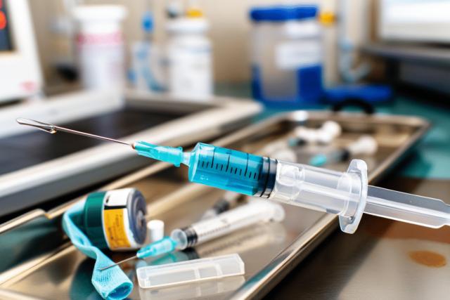 A close-up of a medical syringe with a capped needle resting on a sterile tray, surrounded by subtle hints of other blurred medical equipment in the background, emphasizing the tools used in diagnosing and treating infections.